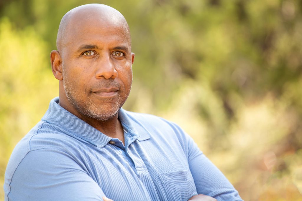 a close-up of a bald, serious-looking, middle-aged man outside