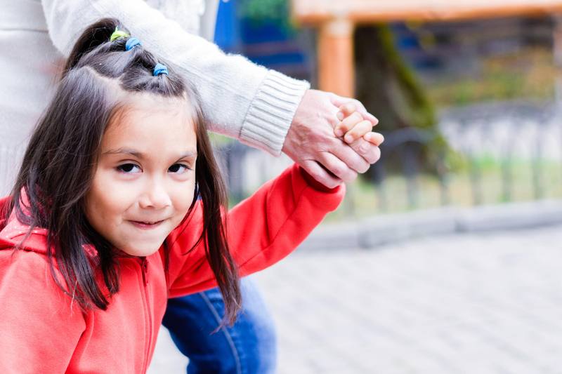 Young girl with a smile walks while holding an adult's hand